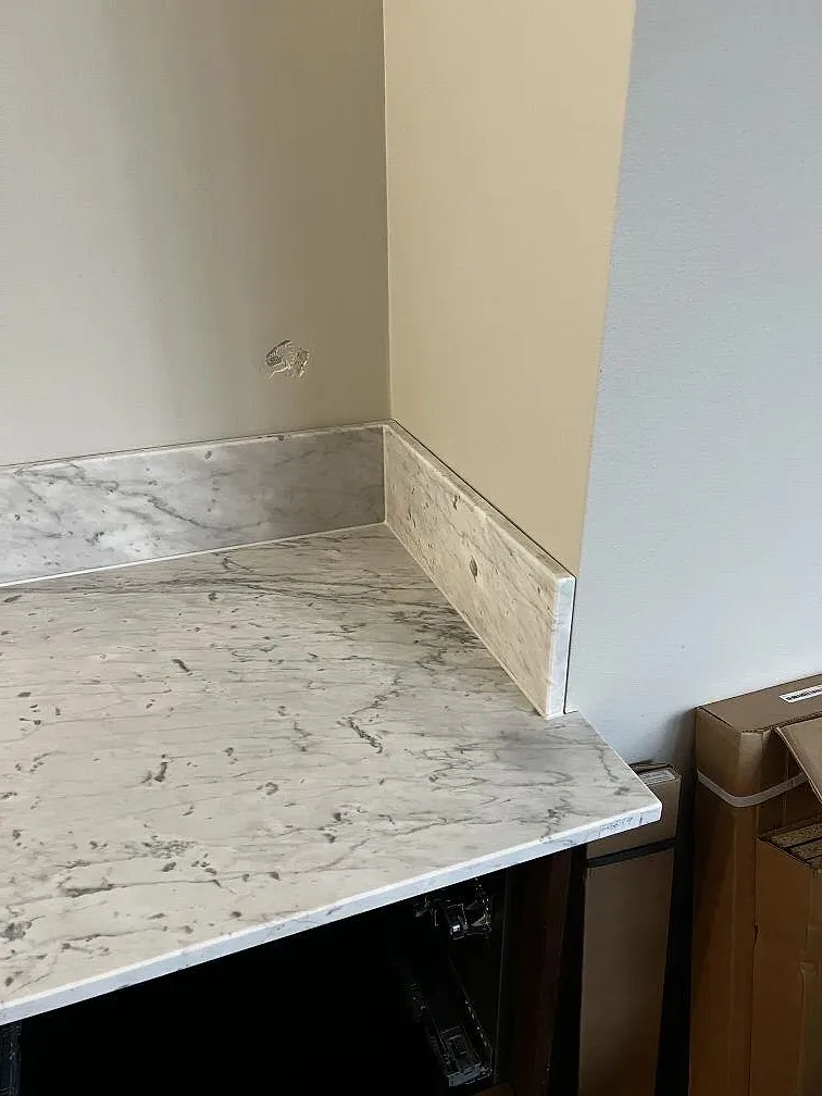 Detalj av uppvikt stänkkant och bänkskiva i Carrara C marmor vid vägg i ett kök i Trelleborg.