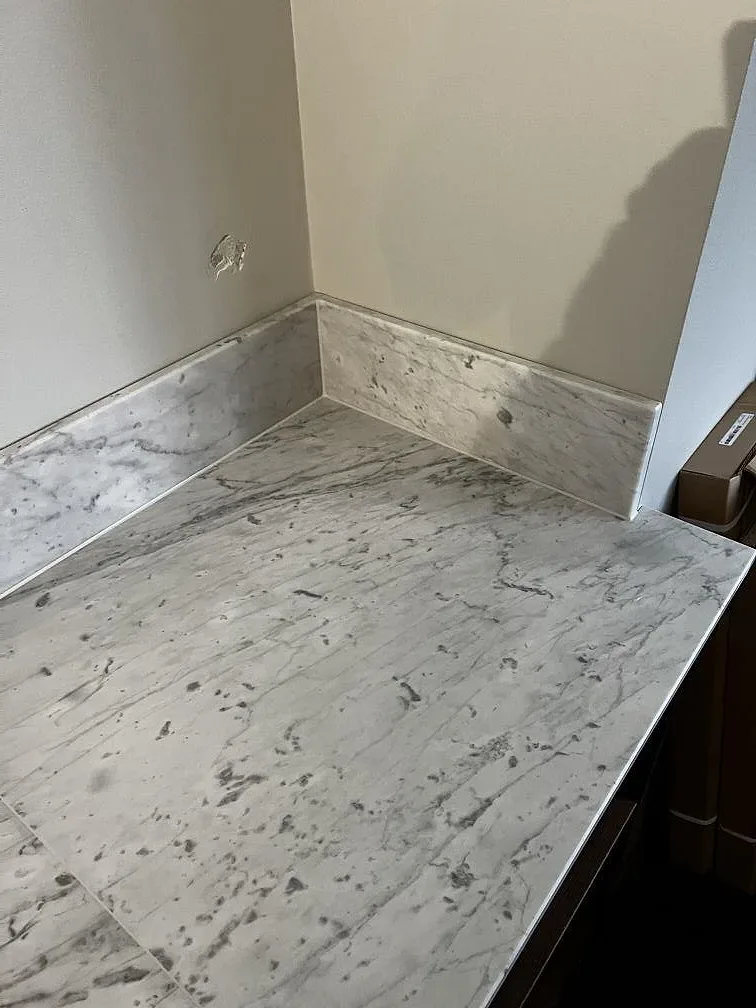 Hörn med uppvikt stänkkant och Carrara C marmorskiva, 20 mm, över mörka köksstommar i Trelleborg.