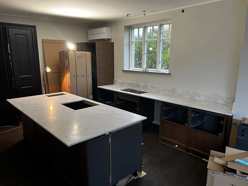 Köksbänkskiva och stor köksö i Carrara C marmor, 20 mm, med mörka stommar och uppvikt stänkkant i Trelleborg.