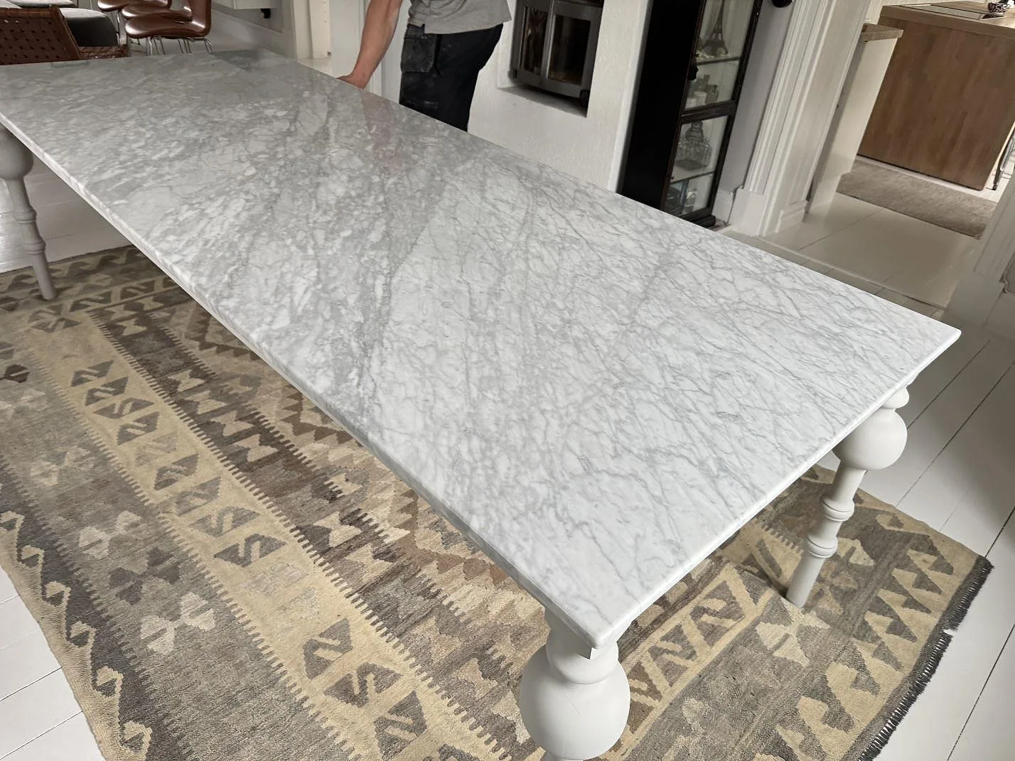 Lång bordsskiva i vit Carrara C marmor, polerad, sedd snett ovanifrån på bordsben i Trollhättan.
