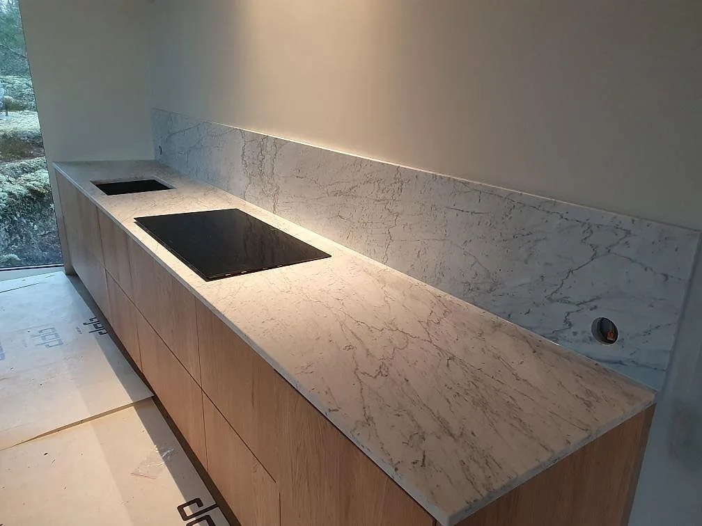 Närmare vy av matt Carrara C marmor på köksbänk med häll och uppvikt stänkskydd i Trosa.