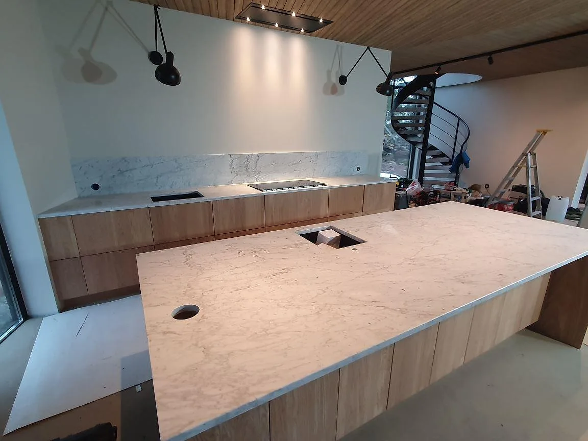 Vinklad vy över köksö och lång köksbänk i matt Carrara C marmor under montering i Trosa.