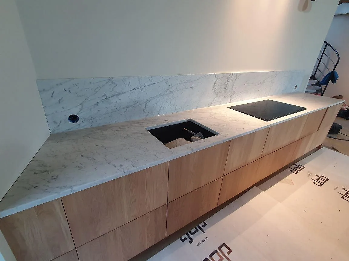 Detalj av väggbänk i matt Carrara C marmor med bearbetad öppning, häll och stänkkant i Trosa.