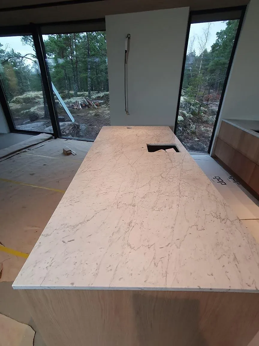Ovanvy av köksö i matt Carrara C marmor med ljus grå ådring under montering i Trosa.