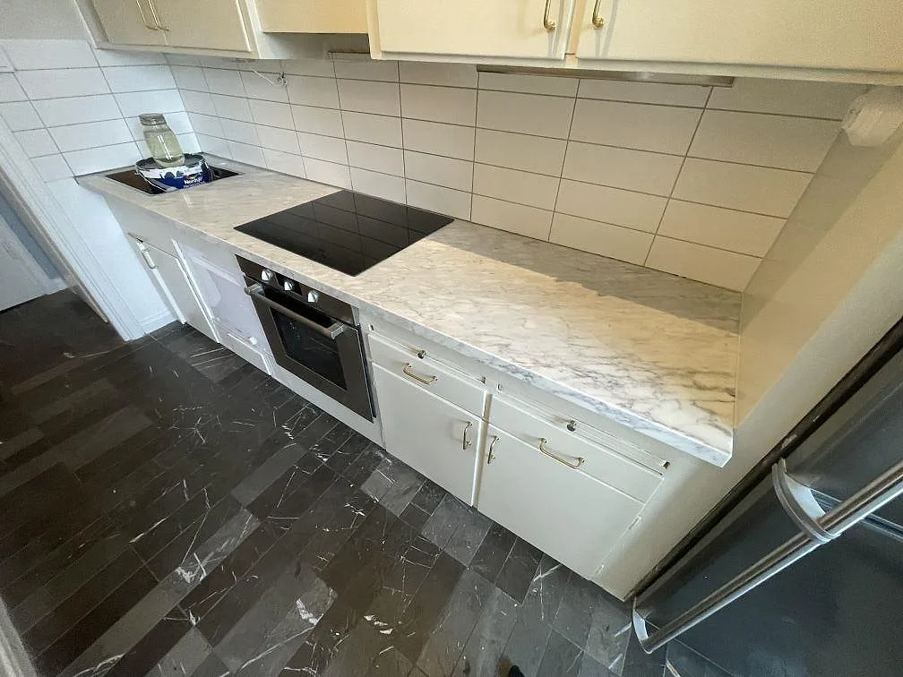 Matt köksbänkskiva i Carrara C marmor längs kaklad vägg med häll och sammanhängande arbetsyta i Uppsala.