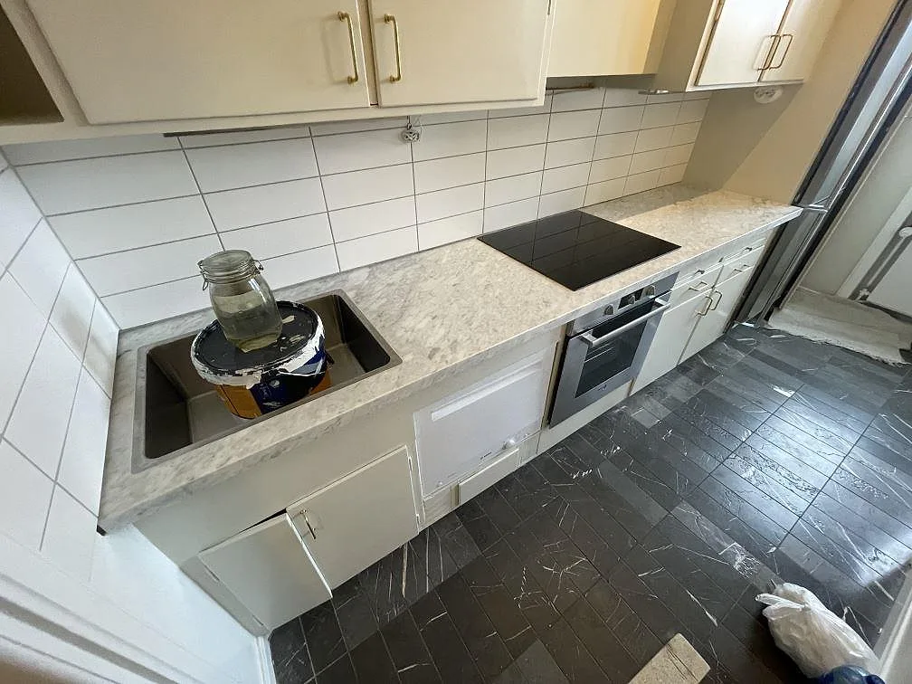 Köksbänkskiva i Carrara C marmor, matt, med synlig diskho och häll i ett kök i Uppsala.