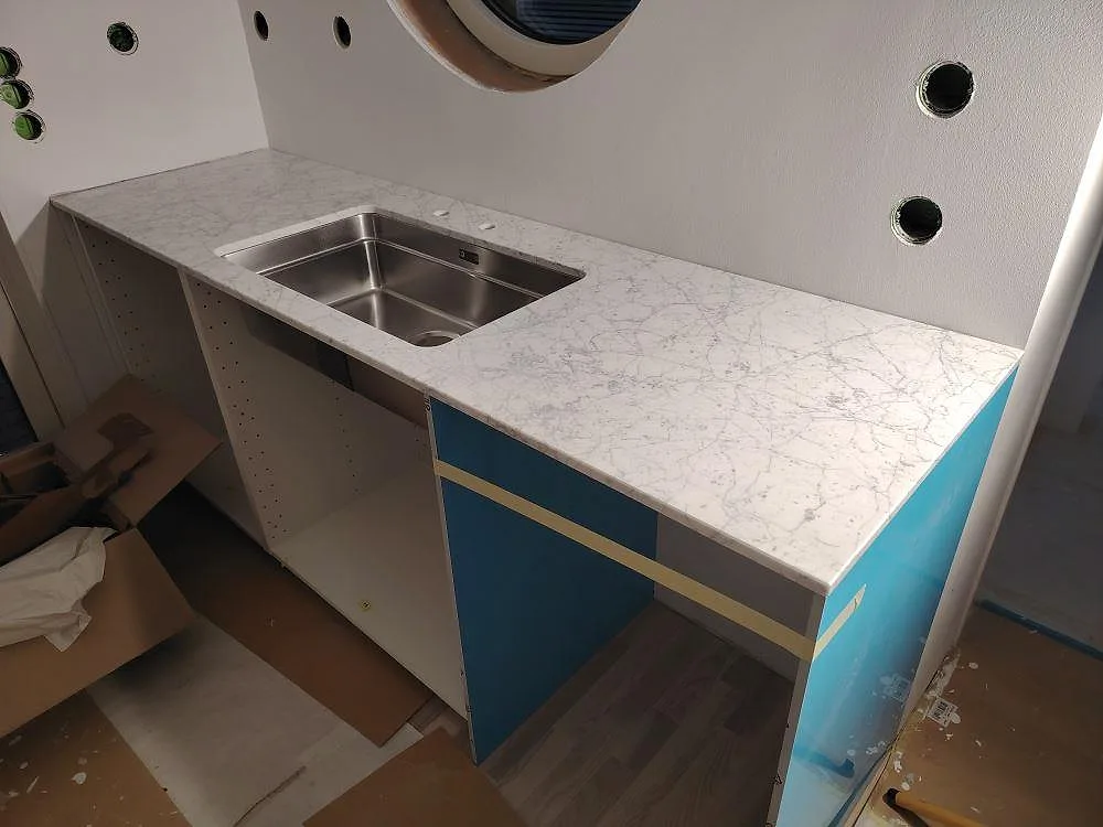 Matt köksbänkskiva i Carrara C marmor med synlig rostfri diskho och grå ådring under montering i Västervik.