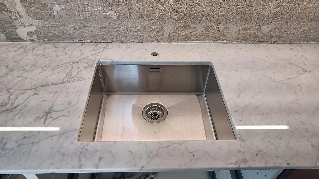 Närbild på rostfri diskho i polerad Carrara C marmor, med tunn grå ådring runt öppningen i Västra Frölunda.