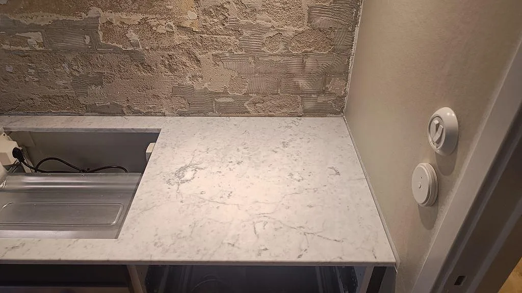 Höger avslutning av polerad Carrara C bänkskiva mot vägg, med ljus marmorering i köket i Västra Frölunda.