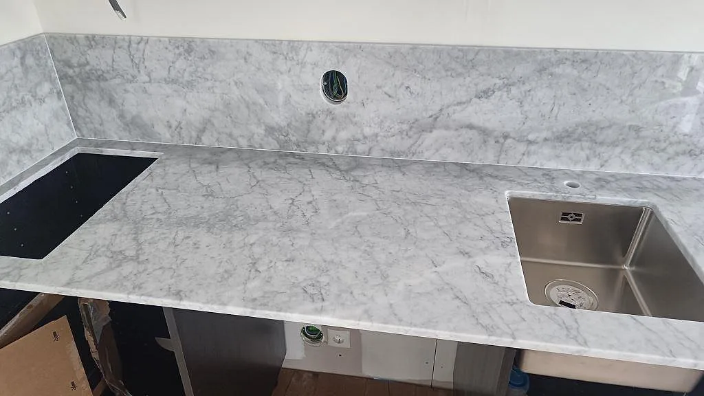Närbild på polerad Carrara C som köksbänkskiva med grå ådring, diskho och stänkkant i Västra Karup.