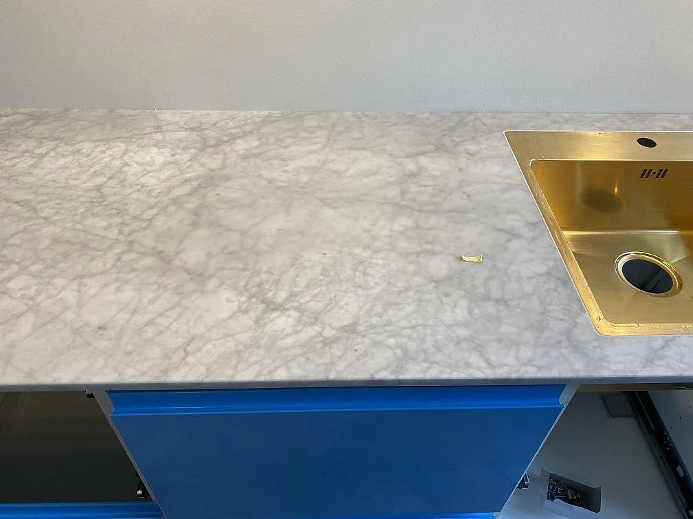 Köksbänkskiva i vit Carrara C marmor med underlimmad diskho i mässingston i ett kök i Valby.