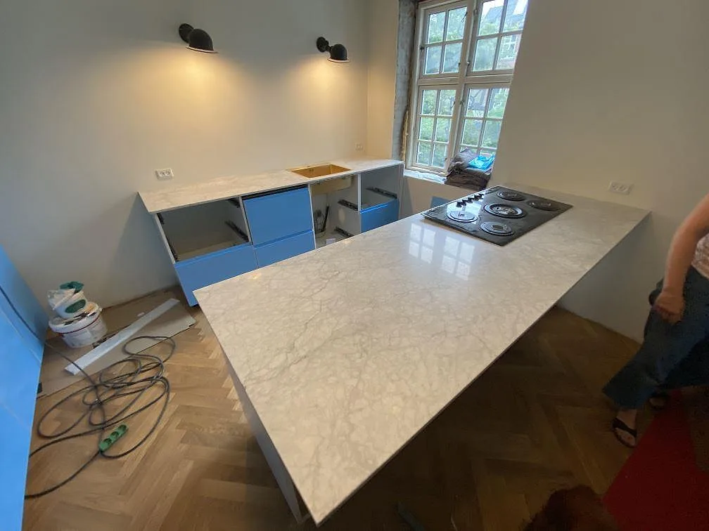 Köksbänkskiva och köksö i vit Carrara C marmor, matt, med installerad gashäll i ett kök under montering i Valby.