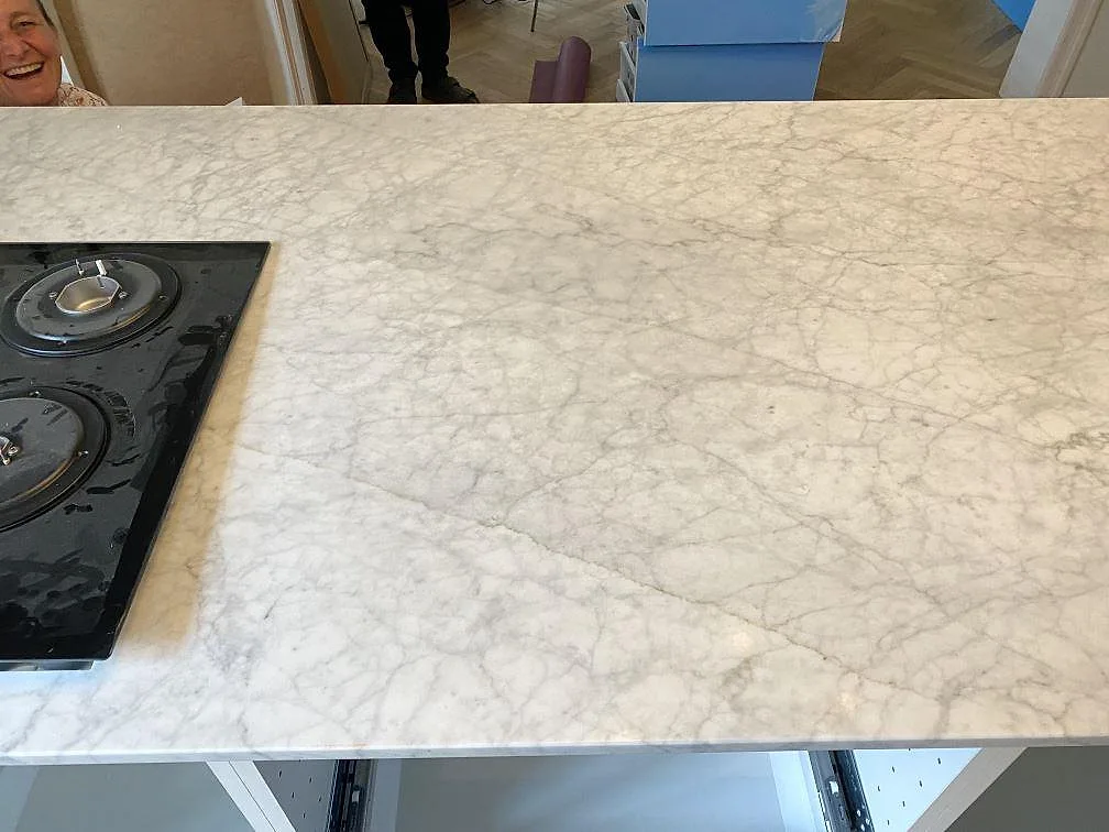 Köksö i vit Carrara C marmor med installerad gashäll och grå ådring i ett kök i Valby.