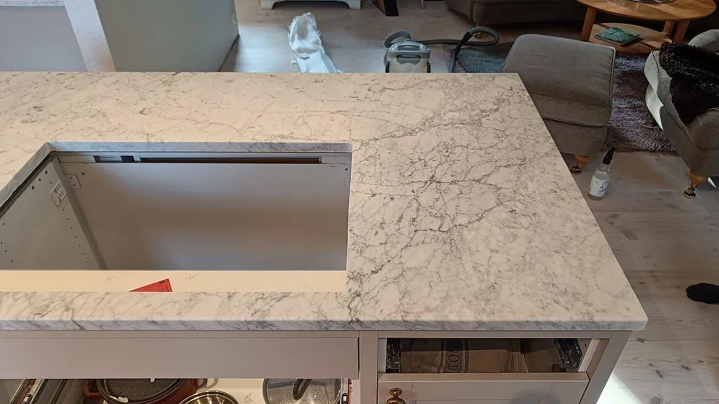 Närbild ovanifrån av köksö i matt Carrara C-marmor med stor rektangulär öppning i Vejbystrand.