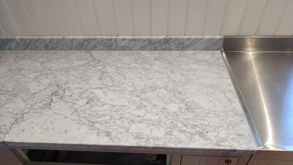 Carrara C marmorbänk som möter integrerad avrinningsyta i rostfritt stål med matchande marmorstänkkant i ett kök i Vejbystrand.