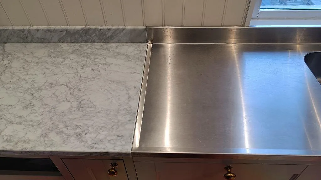 Vit Carrara C marmorbänk bredvid rostfri diskbänk med mässingsknoppar i ett kök i Vejbystrand.