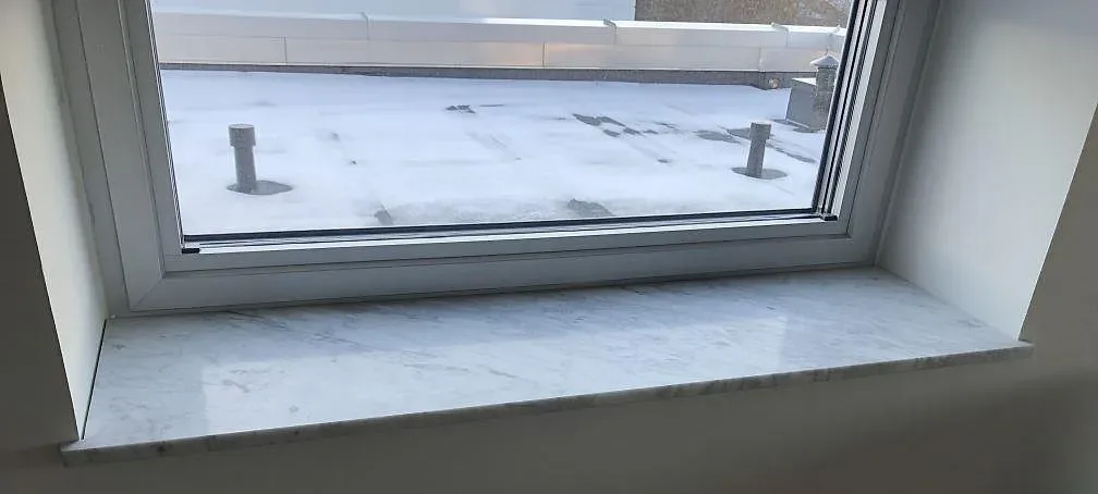 Fönsterbänk i vit Carrara C-marmor, matt yta med mjuk grå ådring, monterad vid ett fönster i ett rum i Ystad.