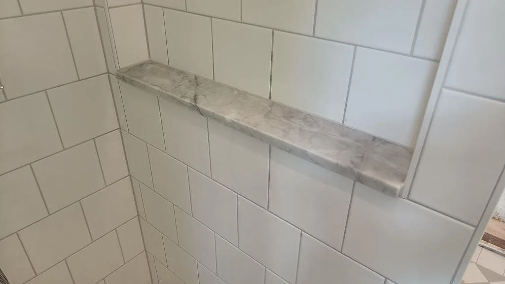 Hylla i Carrara-marmor monterad i en kaklad duschnisch i ett badrum i Höllviken.