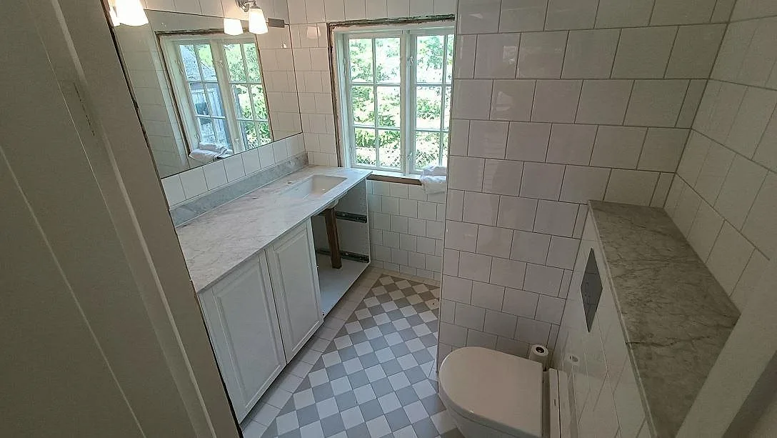 Badrum under montering i Höllviken med vit Carrara-marmor som bänkskiva, vitt kommodskåp och kaklade väggar.