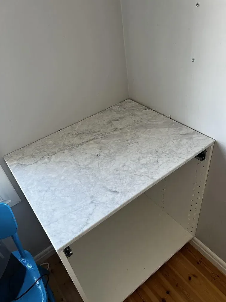 Sidosektion med matt Carrara C marmorskiva monterad på vit köksstomme under pågående montering i Hunnebostrand.