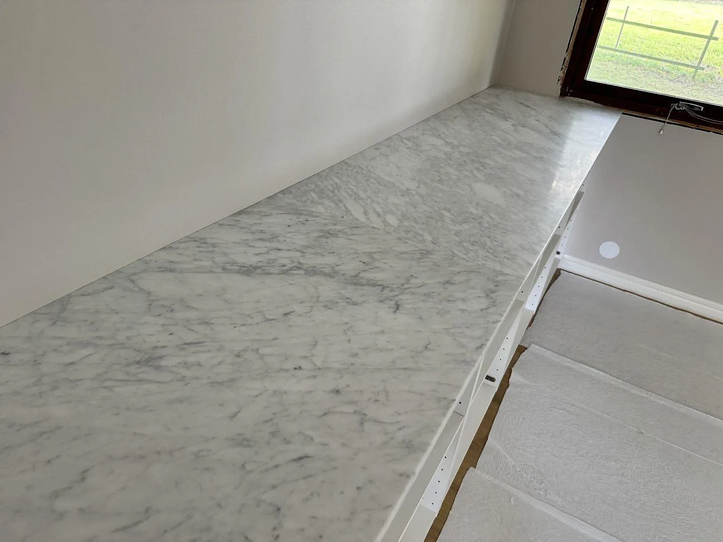 Installerad Carrara C marmorbänkskiva, matt, som löper mot ett fönster i köket i Klippan.