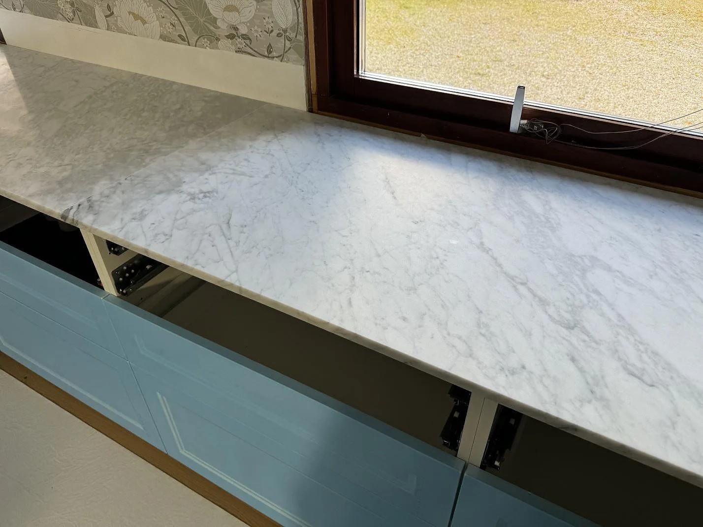 Lång 20 mm bänkskiva i matt Carrara C marmor vid fönster och blå köksstommar i Klippan.