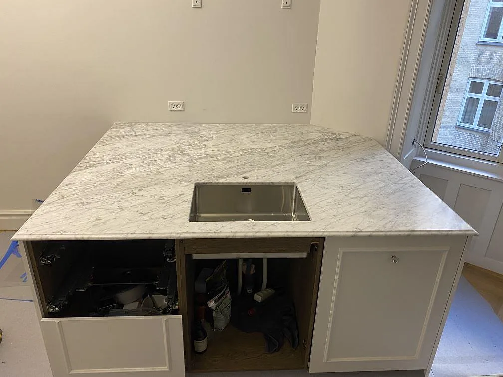 Matt marmorbänkskiva i Carrara C med rostfri diskho och öppna köksstommar under montering i København Ø.