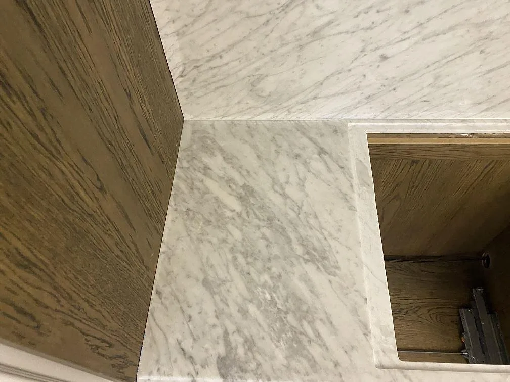 Detalj av matt Carrara C marmor vid hällurtag och träinredd köksnisch i København Ø.