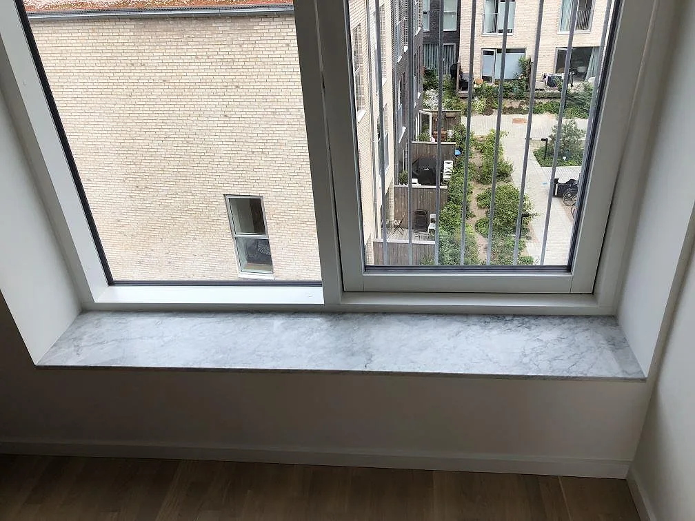 Fönsterbänk i vit Carrara CD-marmor med grå ådring, matt yta, monterad i en ljus lägenhet i København S.