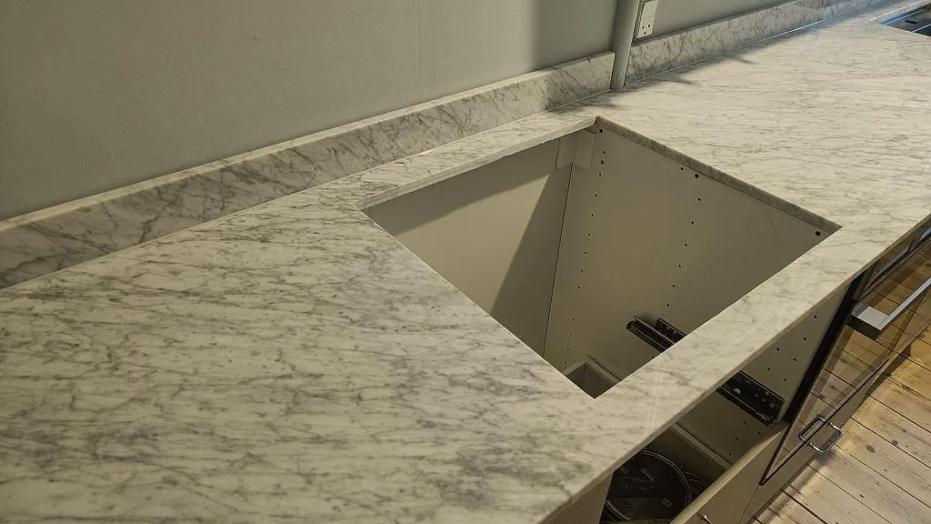 Köksbänkskiva i polerad Carrara C marmor med urtag vid diskzonen och låg stänkkant längs väggen i København S.