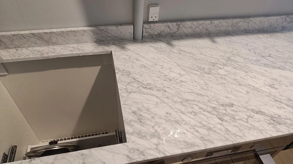 Polerad Carrara C köksbänkskiva med blank marmoryta, låg stänkkant och öppet urtag under montering i København S.