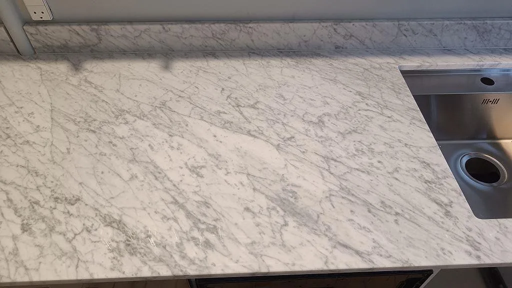 Polerad Carrara C marmoryta med låg stänkkant och rostfri diskho vid kanten av köksbänken i København S.