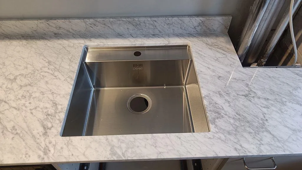 Underlimmad rostfri diskho i polerad Carrara C marmorbänkskiva med grå ådring och vit skåpinredning i København S.