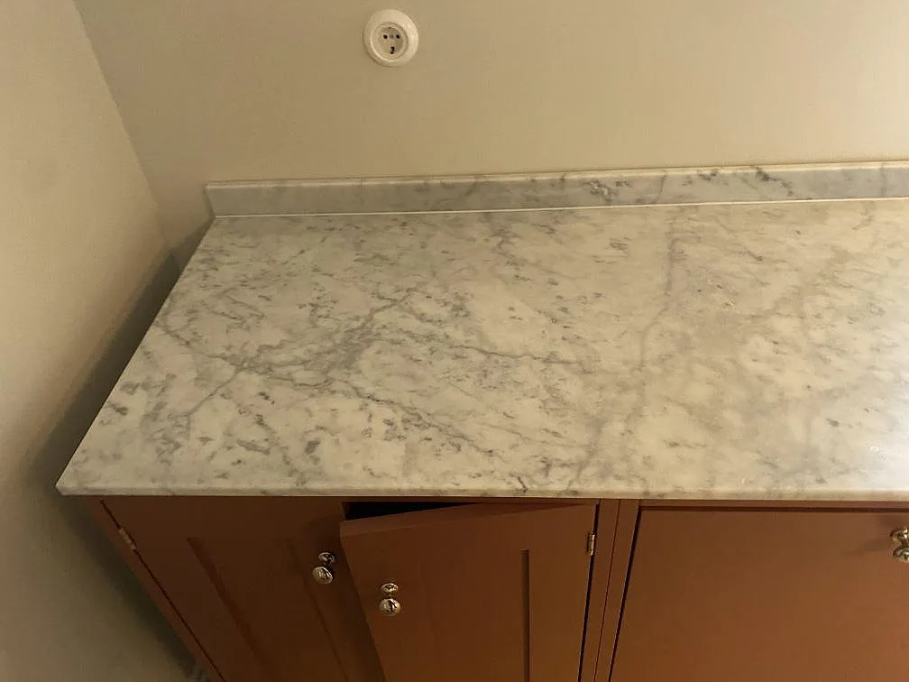 Köksbänkskiva i matt Carrara CD-marmor med uppvikt stänkkant på terrakottafärgade köksstommar i ett kök i Limhamn.