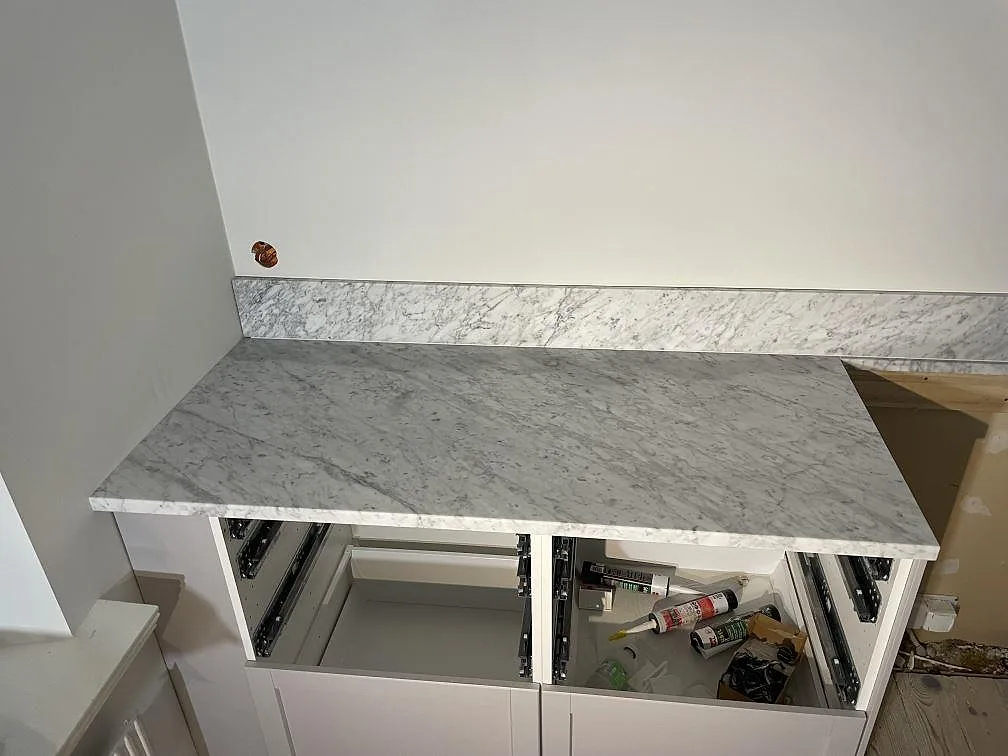 Vänster bänksträcka i matt Carrara C, monterad på öppna köksstommar med stänkskydd i samma marmor i Lund.