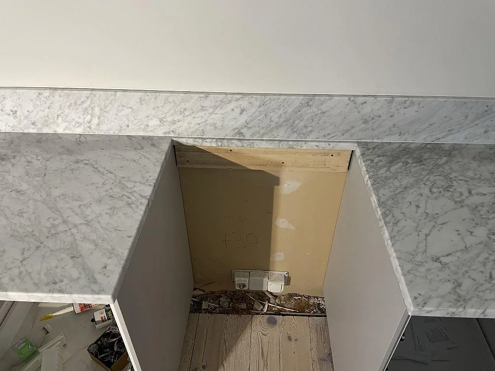 Detalj av Carrara C-bänkskivor runt en öppen apparatplats med stänkskydd i samma marmor i Lund.