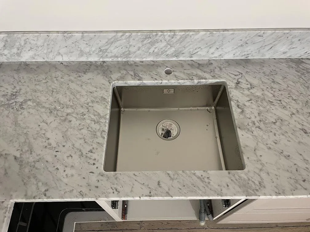Närbild av diskhozonen i matt Carrara C-marmor med stänkskydd bakom bänkskivan i Lund.