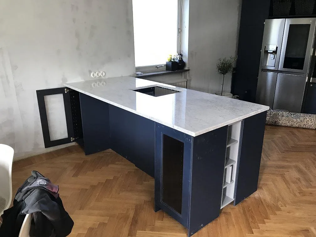 Köksbänkskiva i vit Carrara CD marmor med grå ådring monterad på en marinblå halvö i ett kök under montering i Malmö.
