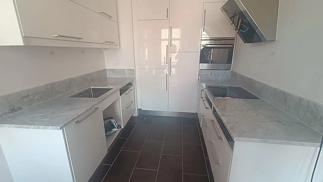 Köksbänkskiva i vit Carrara CD-marmor, polerad, med grå ådring längs båda bänkraderna i ett kök i Malmö.