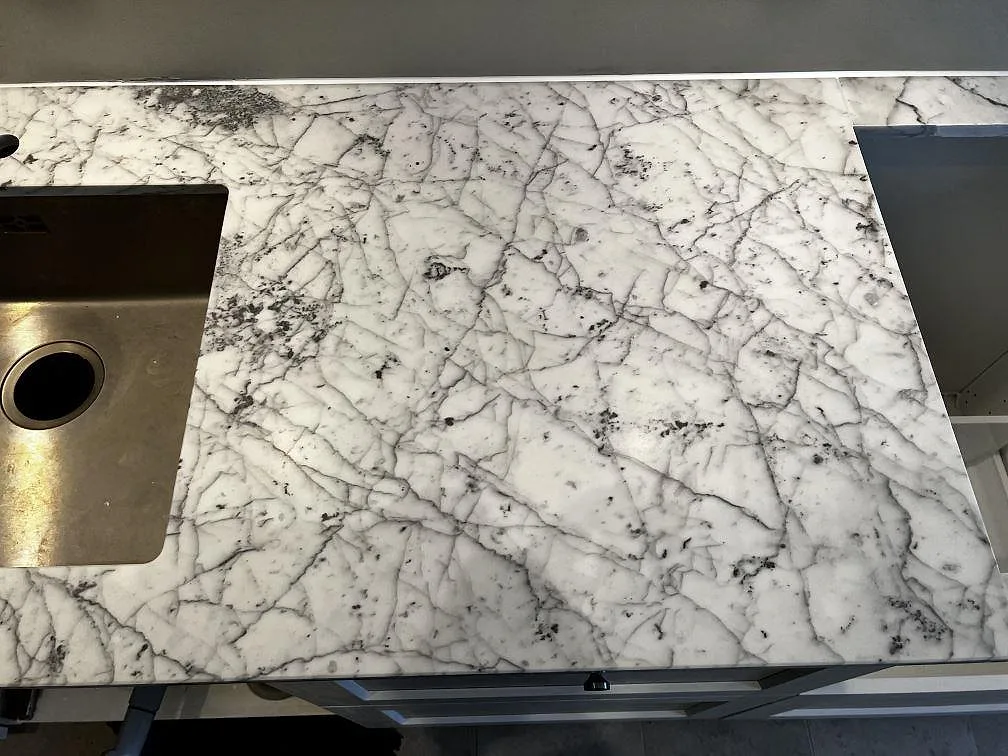 Detalj av matt Carrara C marmorbänkskiva med rostfri diskho och hälluttag i köket i Malmö.