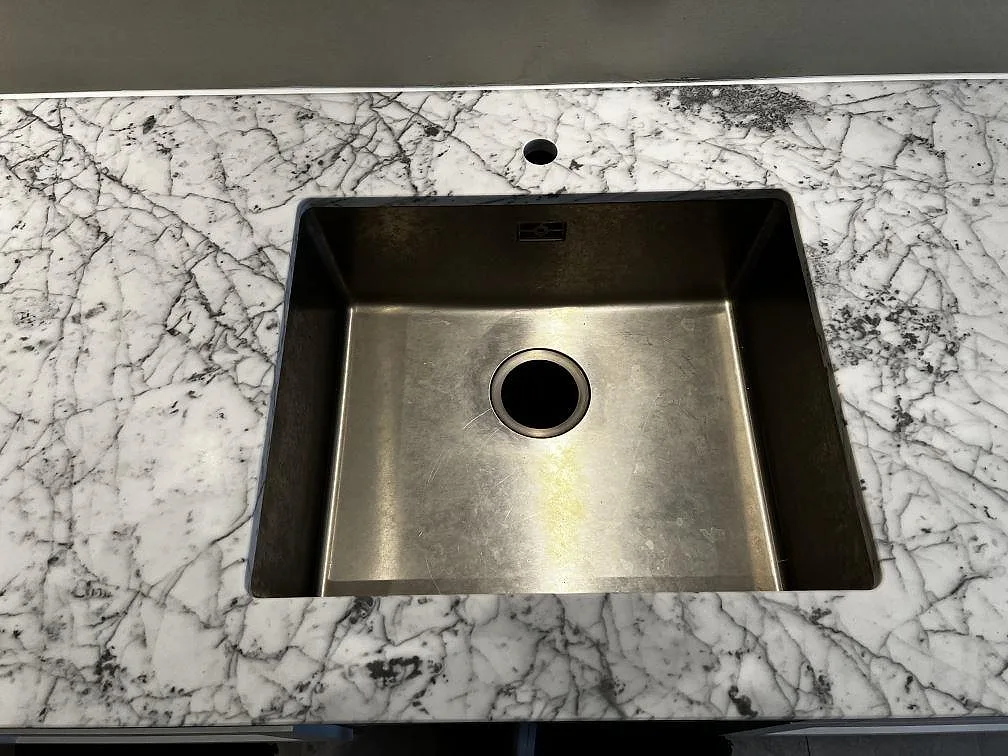 Matt Carrara C marmor runt en underlimmad rostfri diskho i ett kök under montering i Malmö.