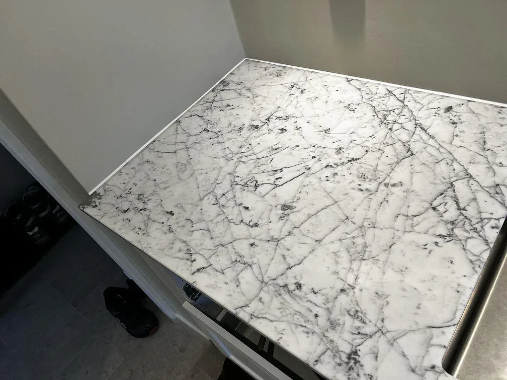 Hörnbit av matt Carrara C marmor på grå köksstommar bredvid rostfri diskho i Malmö.