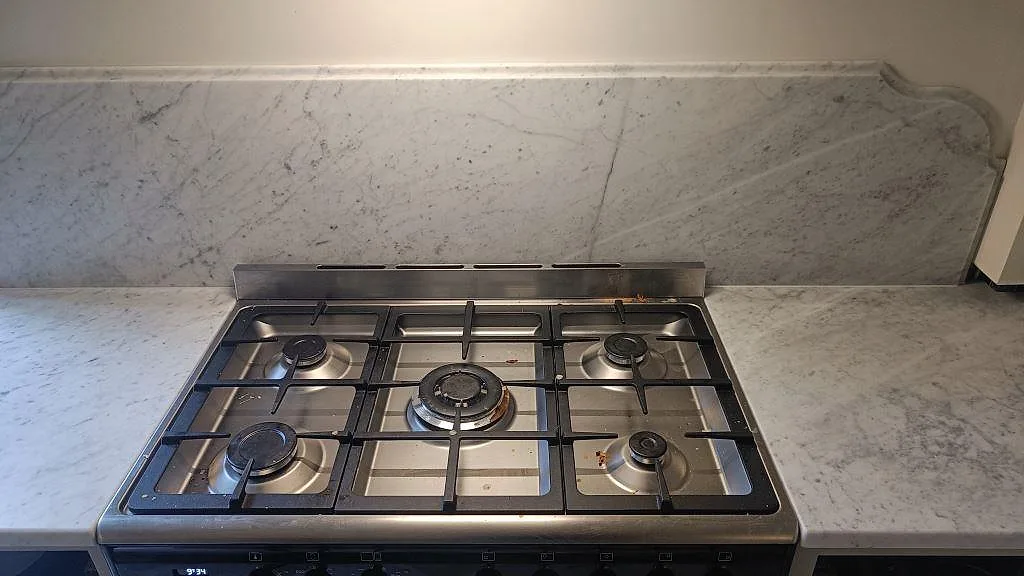 Matt Carrara C marmor runt en fristående gasspis, med bänkskivor på båda sidor och marmorstänkkant i Malmö.