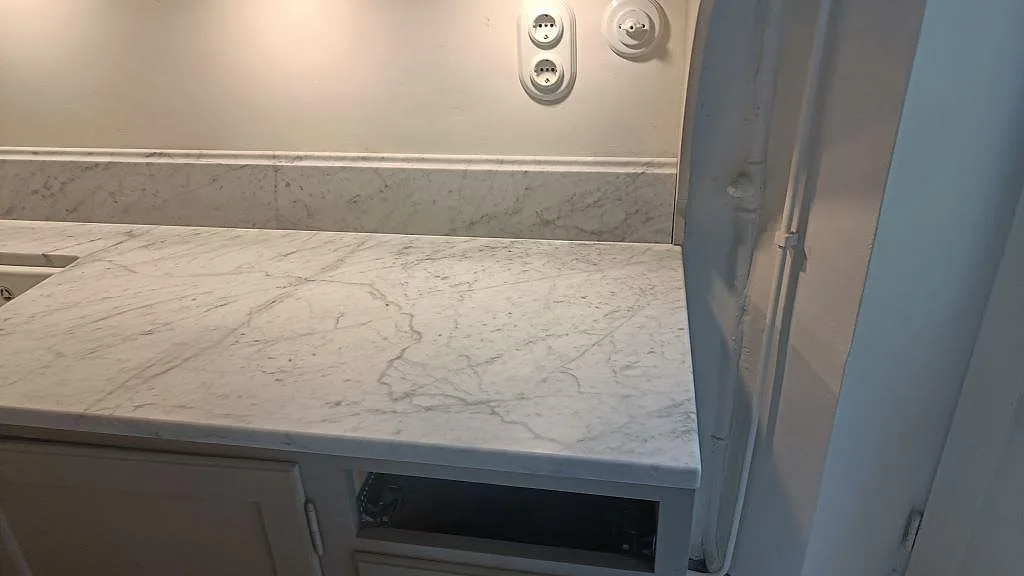 Höger bänkdel i matt Carrara C marmor med synlig ådring, låg marmorstänkkant och vägguttag i Malmö.
