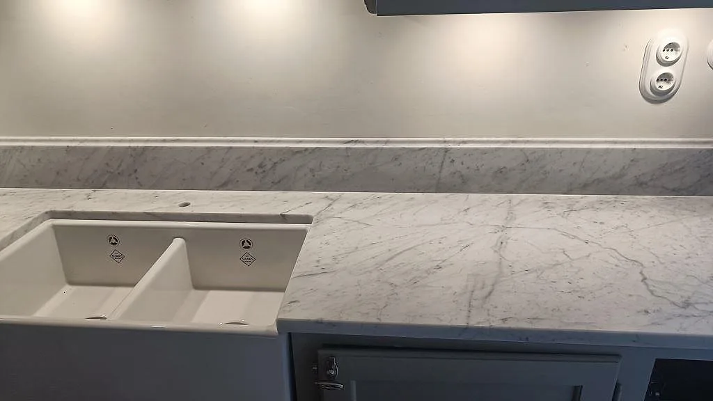 Närbild på matt Carrara C marmorbänkskiva vid diskho och låg stänkkant i ett kök i Malmö.