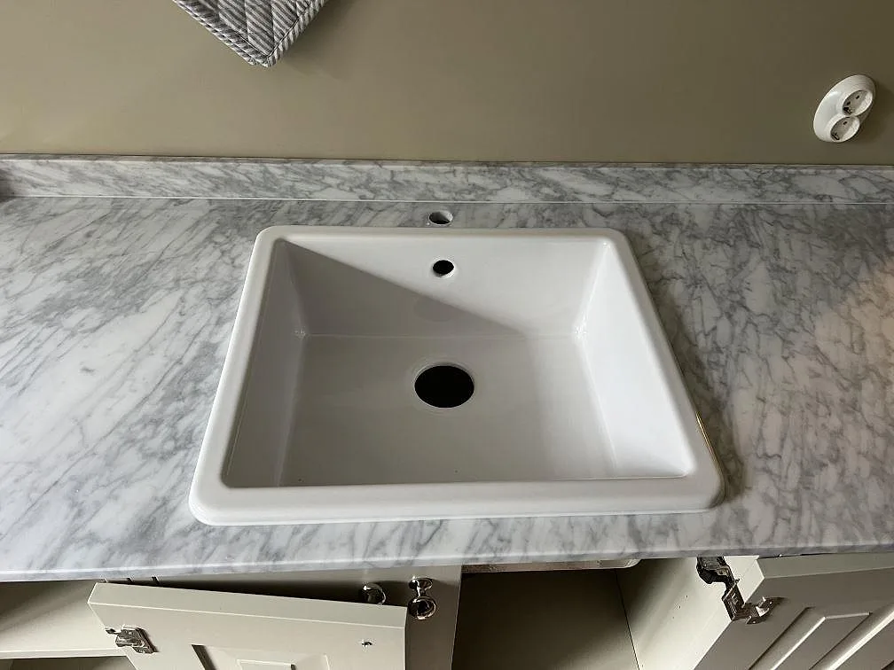 Närbild på vit keramisk diskho ovanpå köksbänkskiva i matt Carrara C marmor i Malmö.