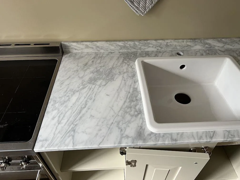 Köksbänkskiva i matt Carrara C marmor i Malmö med vit diskho, spiszon och låg stänkkant.