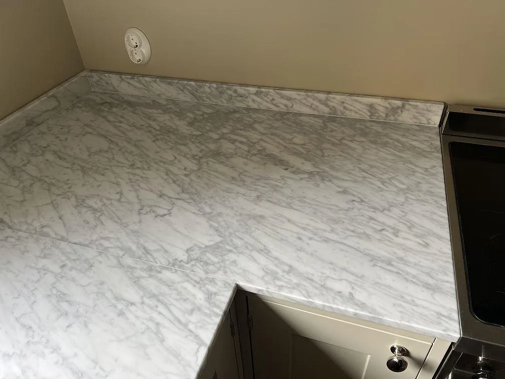 Arbetsyta i matt Carrara C marmor i Malmö med grå ådring, låg stänkkant och spis intill.