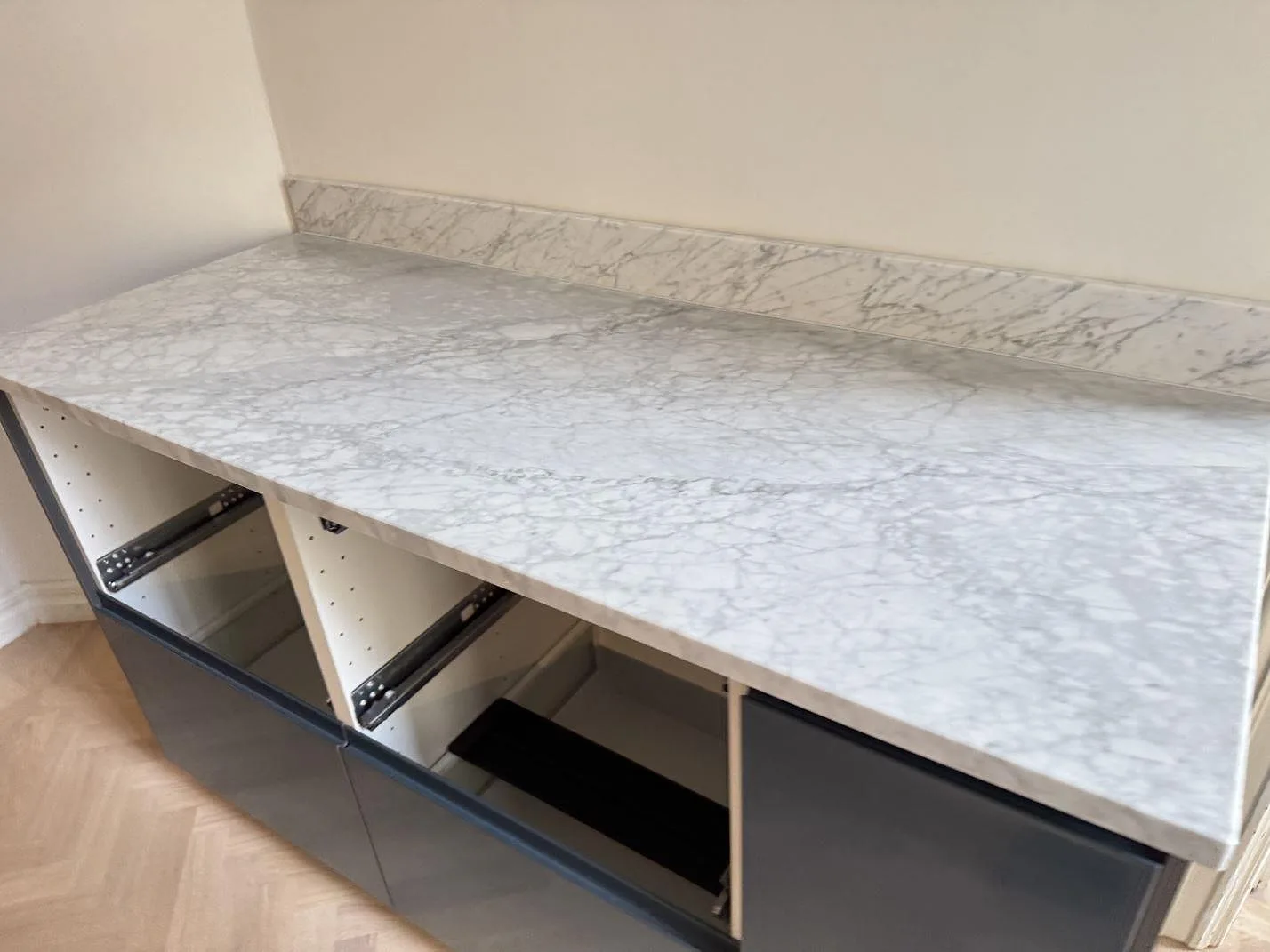 Bänkskiva i matt Carrara C-marmor med uppvikt stänkkant på mörka skåpstommar i Malmö.