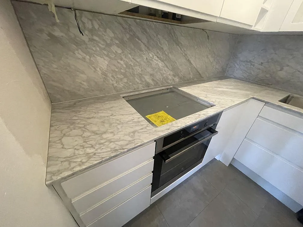 Närbild av matt Carrara C marmorbänkskiva i Örebro med hällzon, ådrat stänkskydd och vita köksskåp.